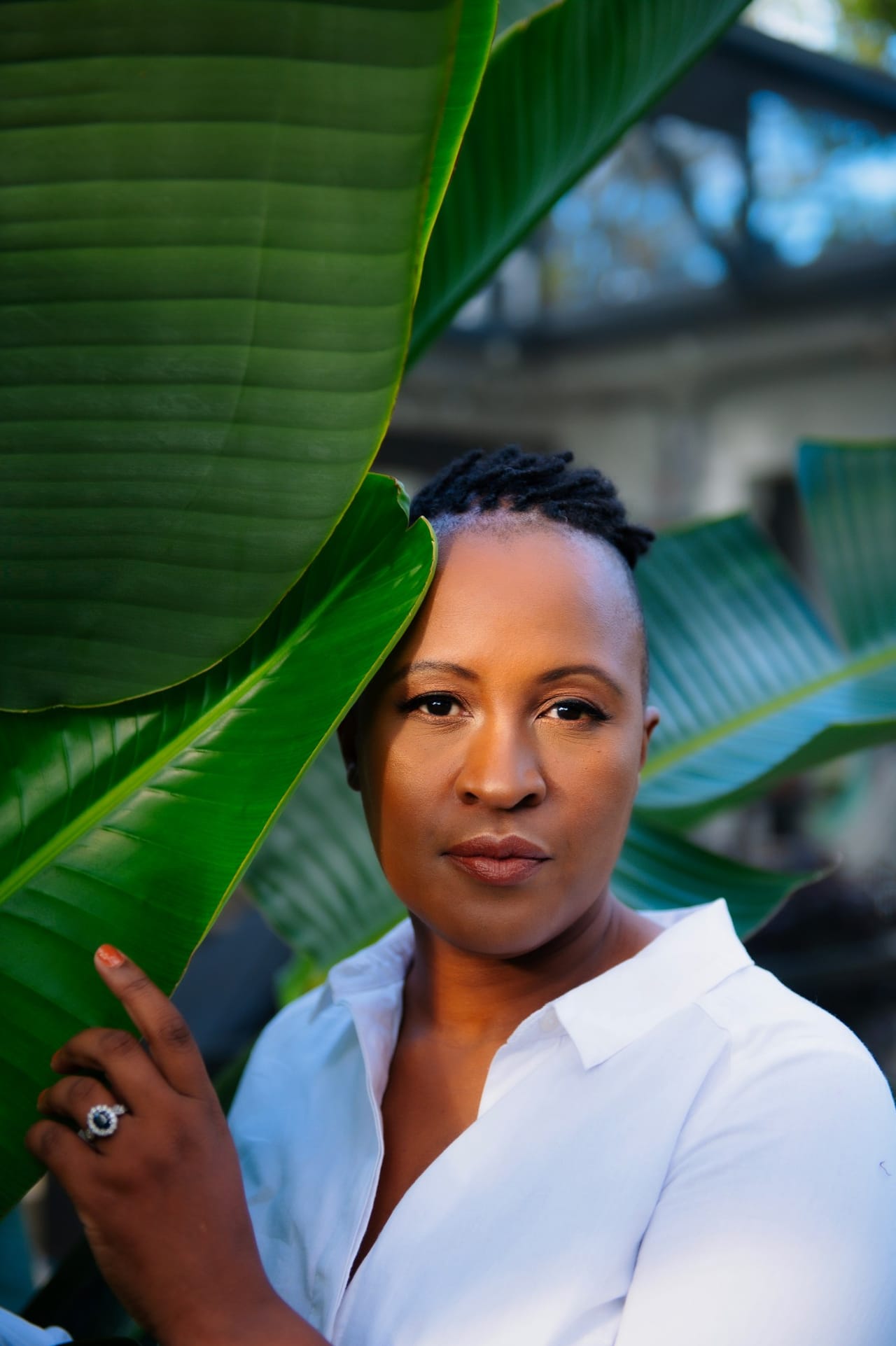 One of the women who runs Booths and Such Rentals, in a white shirt, standing outdoors beside a large tropical leaf